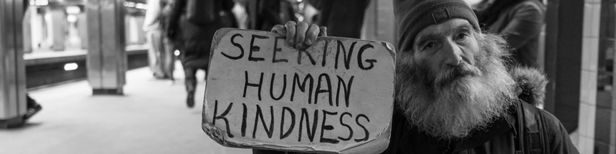 Homeless man holding sign saying 'Seeking human kindness'